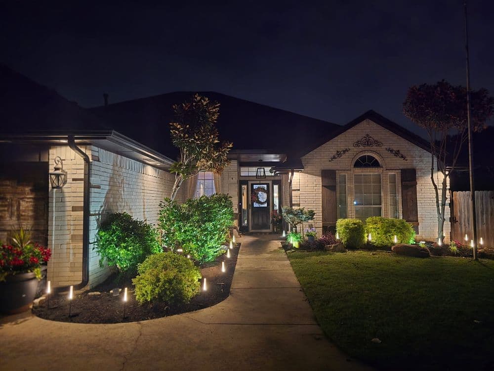 Elegant brick home with garden lighting and lush landscaping at night.