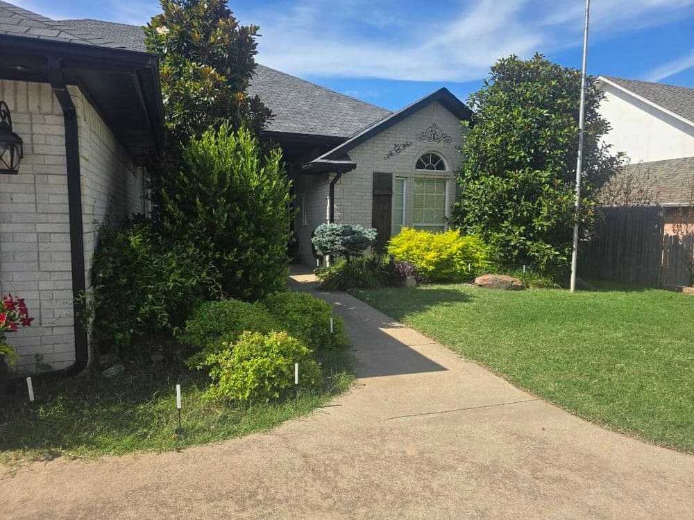 Charming brick house with landscaped front yard and vibrant greenery, sunny day.