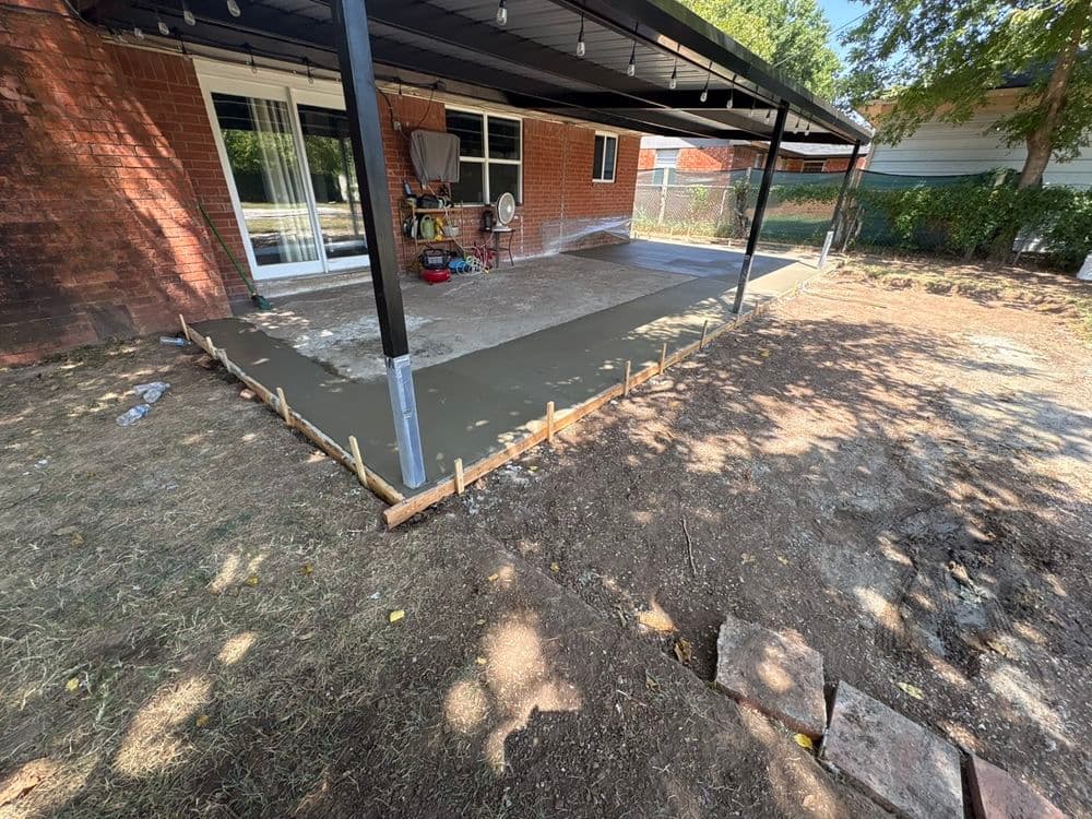 Freshly poured concrete patio extension under covered porch in residential backyard.
