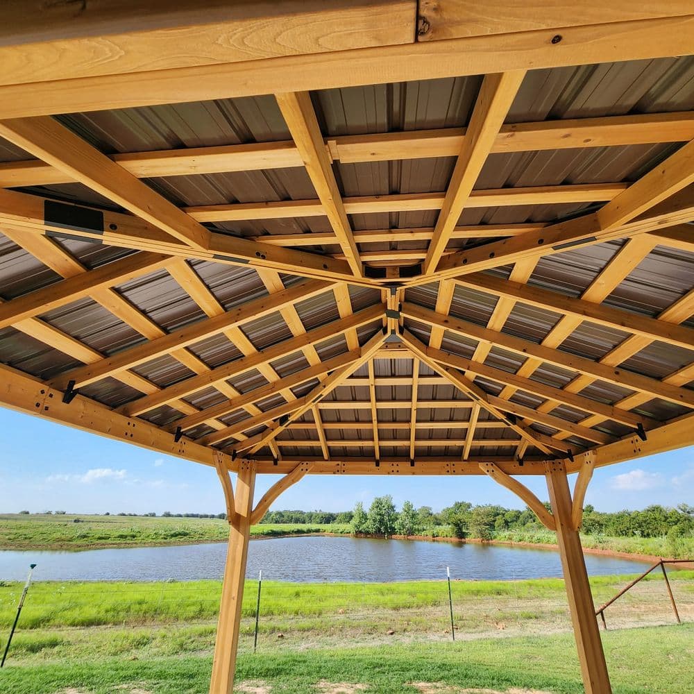 Wooden gazebo roof structure with a view of a serene lake and lush greenery.