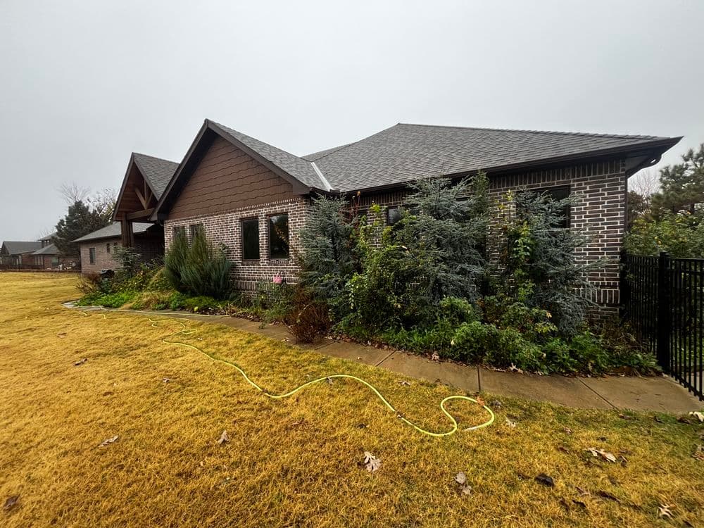Modern brick house with lush landscaping and wet concrete path on a cloudy day.