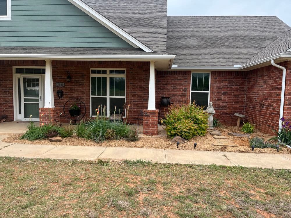Front porch of a home with brick exterior, decorative statue, and landscaped flower beds.