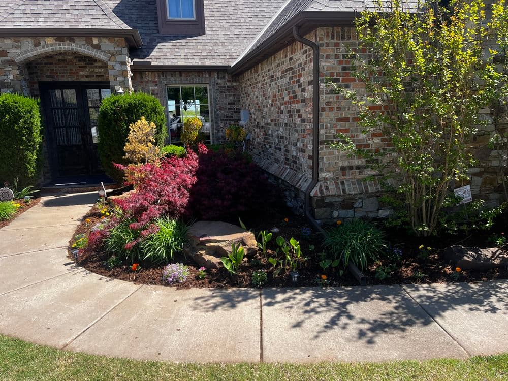 Landscaped front yard with colorful flowers, shrubs, and stone walkway near brick home.