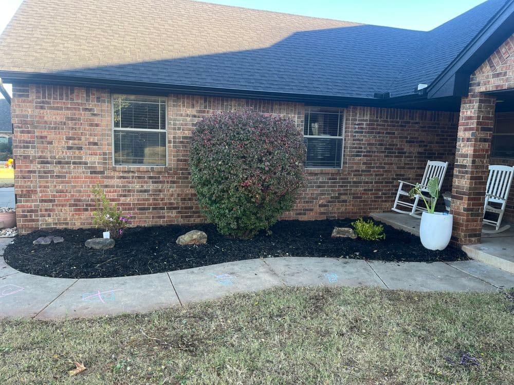 Brick house with landscaped garden featuring shrubs, rocks, and freshly laid mulch.
