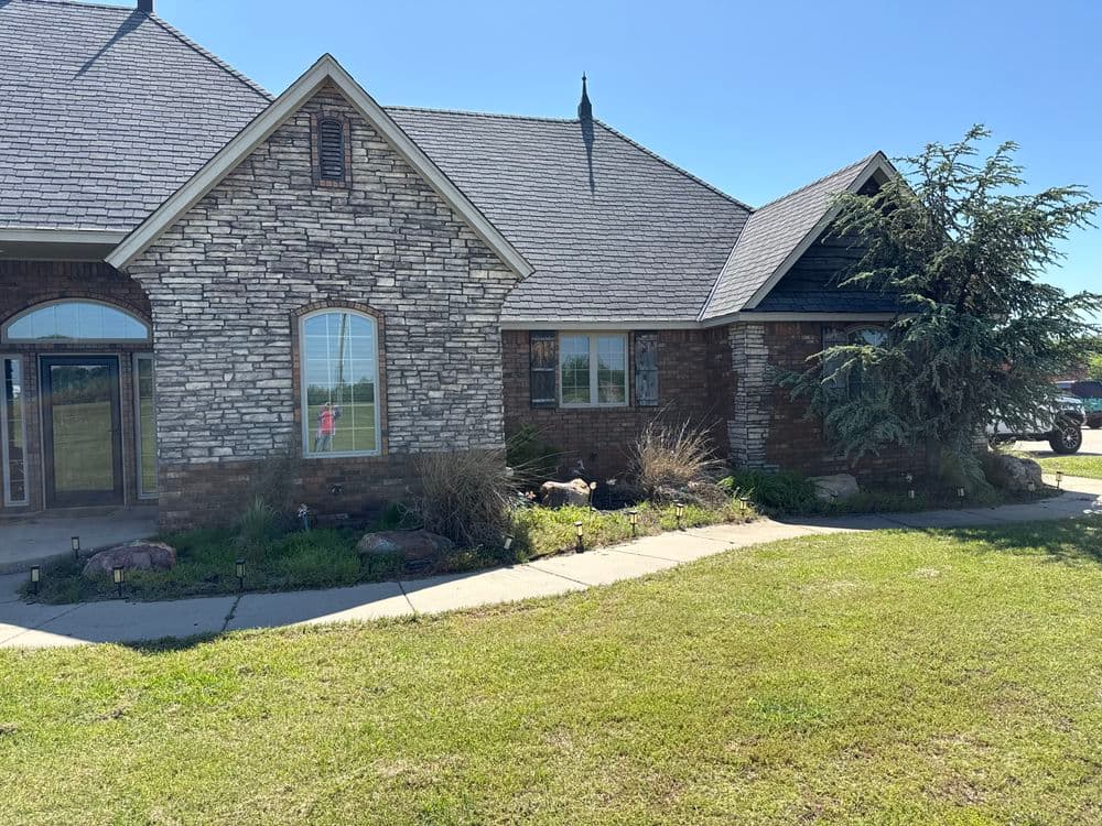 Front view of a stone and brick house with a landscaped yard and clear blue sky.