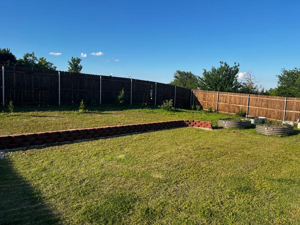 Spacious backyard with green grass, wooden fence, and raised garden beds.