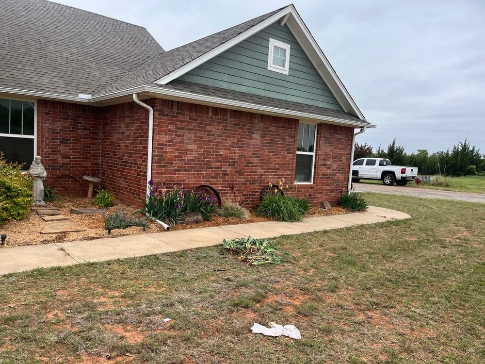 Brick house exterior with flower garden, statue, and white pickup truck parked nearby.