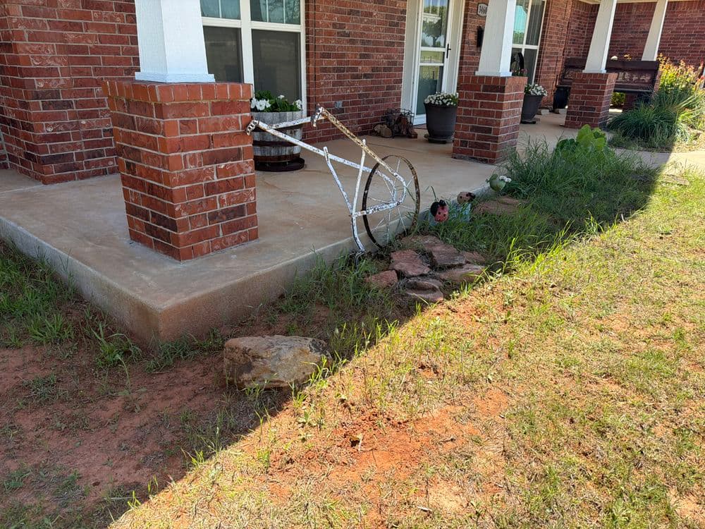 Old white bicycle wheel leaning against brick pillar in grassy yard.