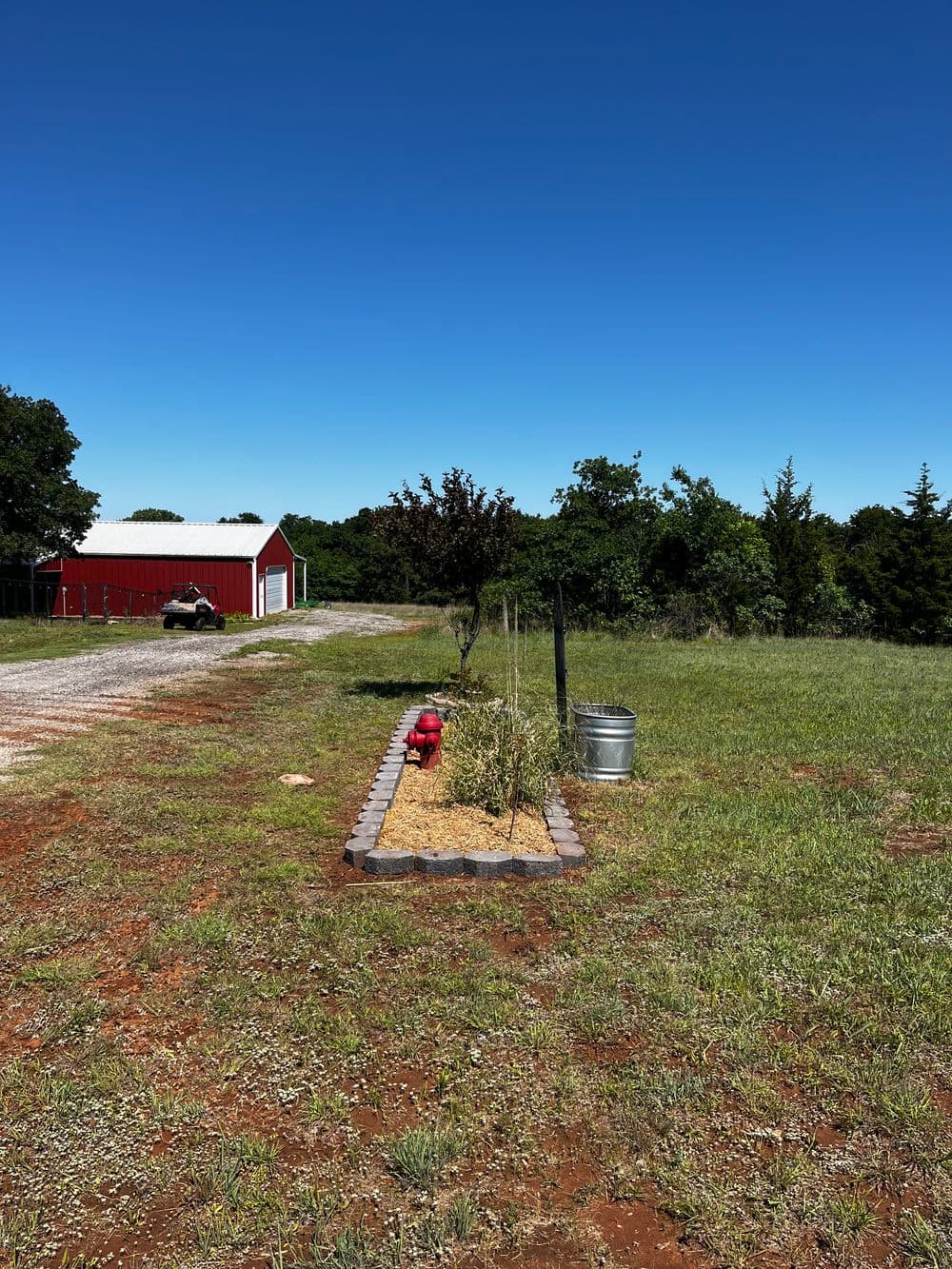 Farm landscape with red barn, fire hydrant, and landscaped garden under a clear blue sky.