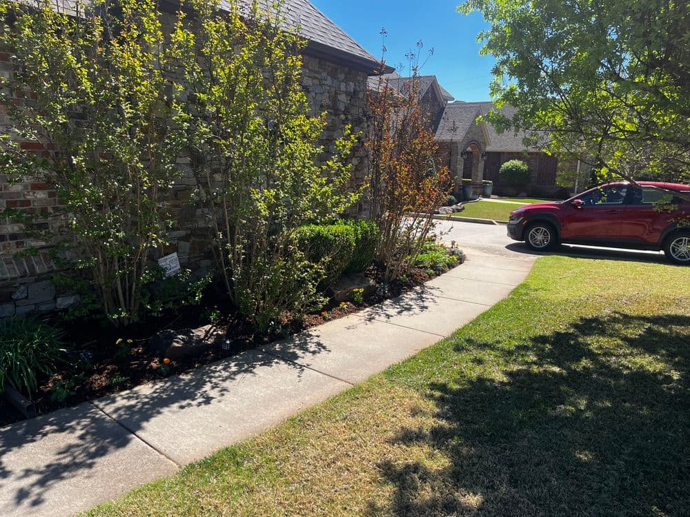 Landscape view of a stone house with a manicured garden and a red SUV parked nearby.