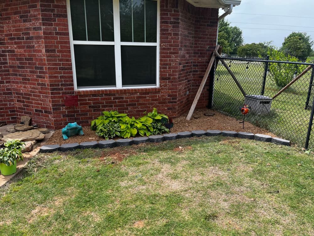 Landscape design featuring plants, stone edging, and a fence in a backyard setting.