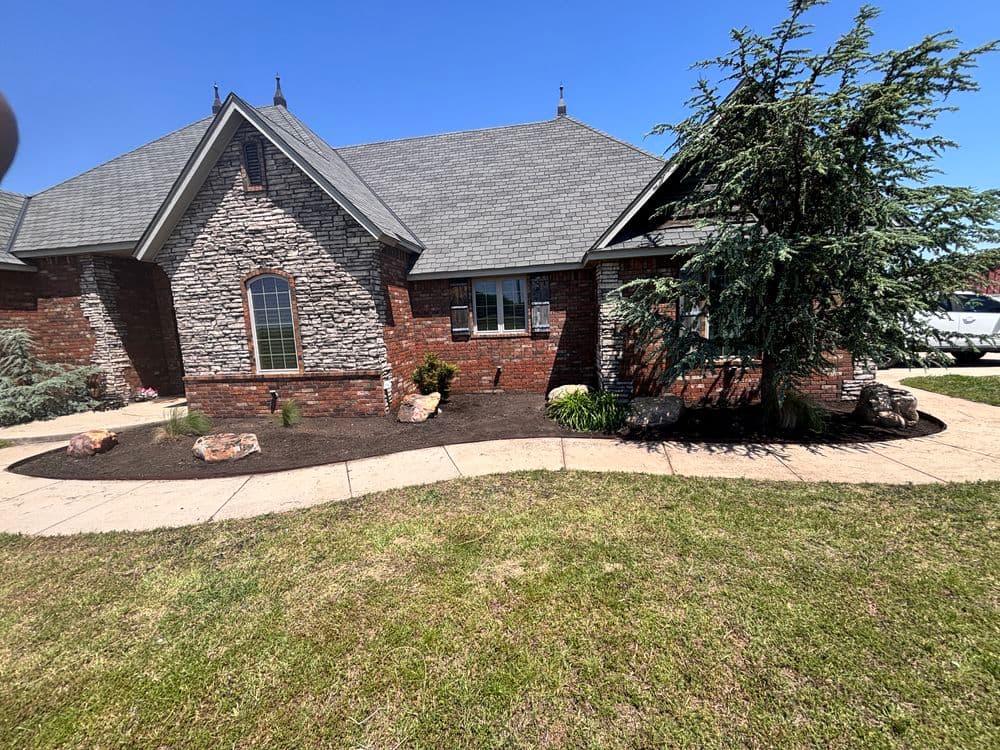 Exterior view of a brick home with stone accents, landscaped yard, and clear blue sky.