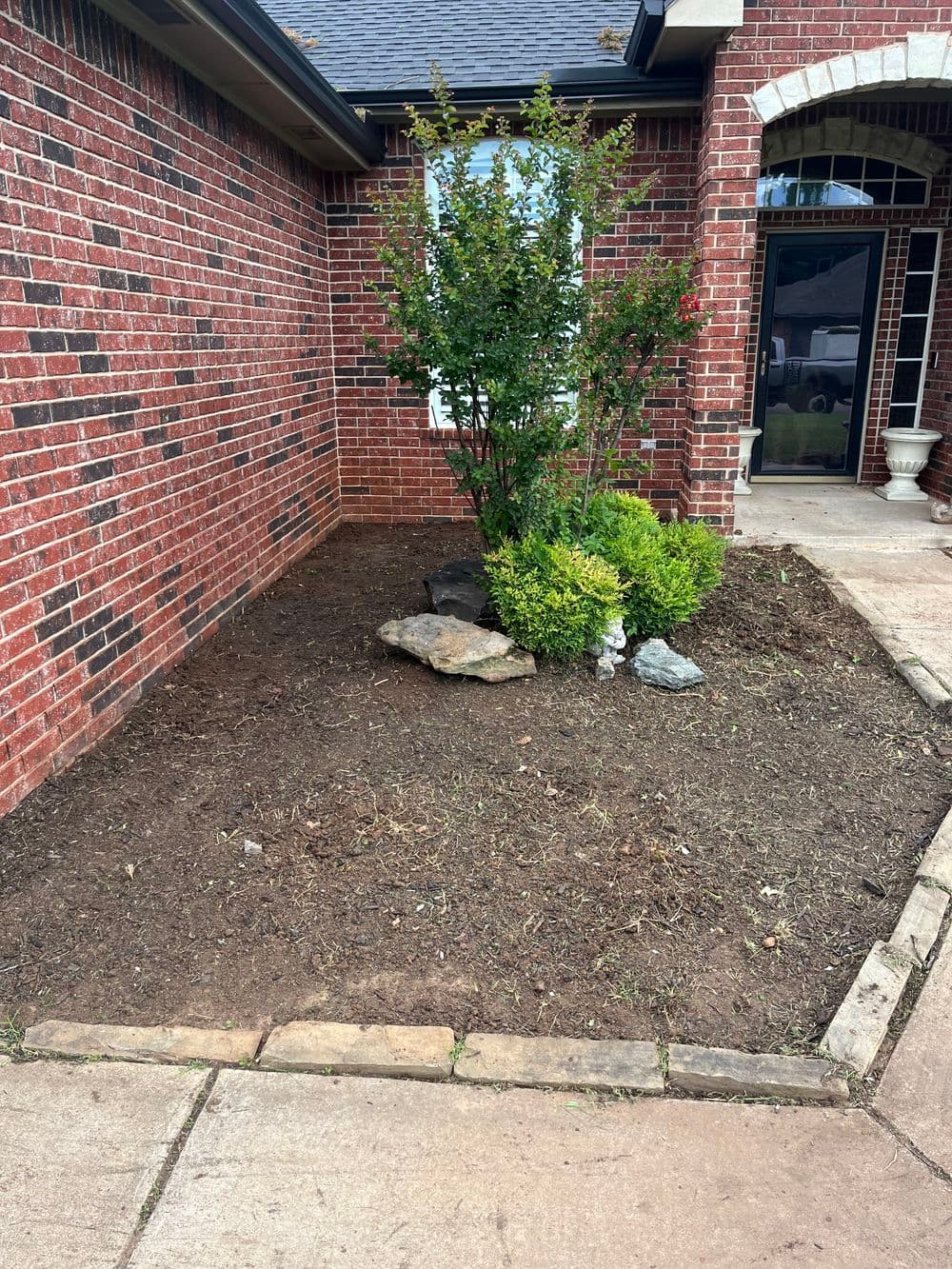 Landscaped yard with brick exterior, shrubbery, rocks, and clear walkway.