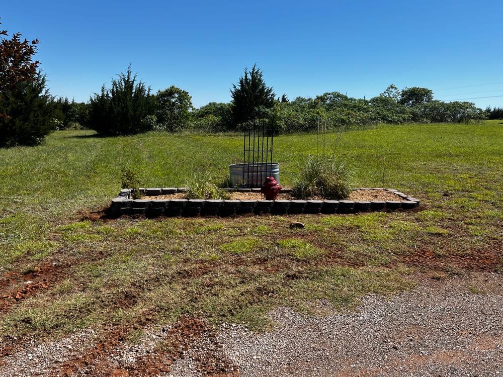 Landscape with decorative flower bed, red fire hydrant, and lush green grass under blue sky.