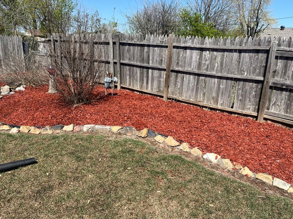 Vibrant red mulch landscaping with wooden fence and bare shrubs in residential backyard.