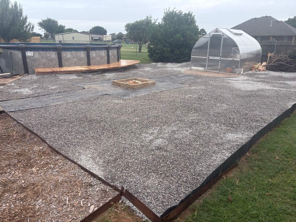 Gravel landscape with a greenhouse and wooden deck in a residential backyard setting.